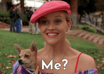 Reese Witherspoon Comedy GIF By Coolidge Corner Theatre - Woman dressed in pink, holding a little dog, and looking surprised while asking "me?".